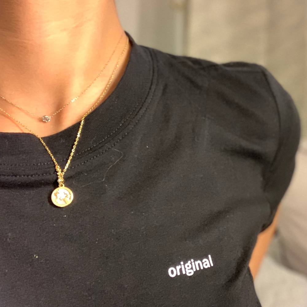 Gold Zodiac necklace worn solo over a black tee — a simple, powerful statement of identity.