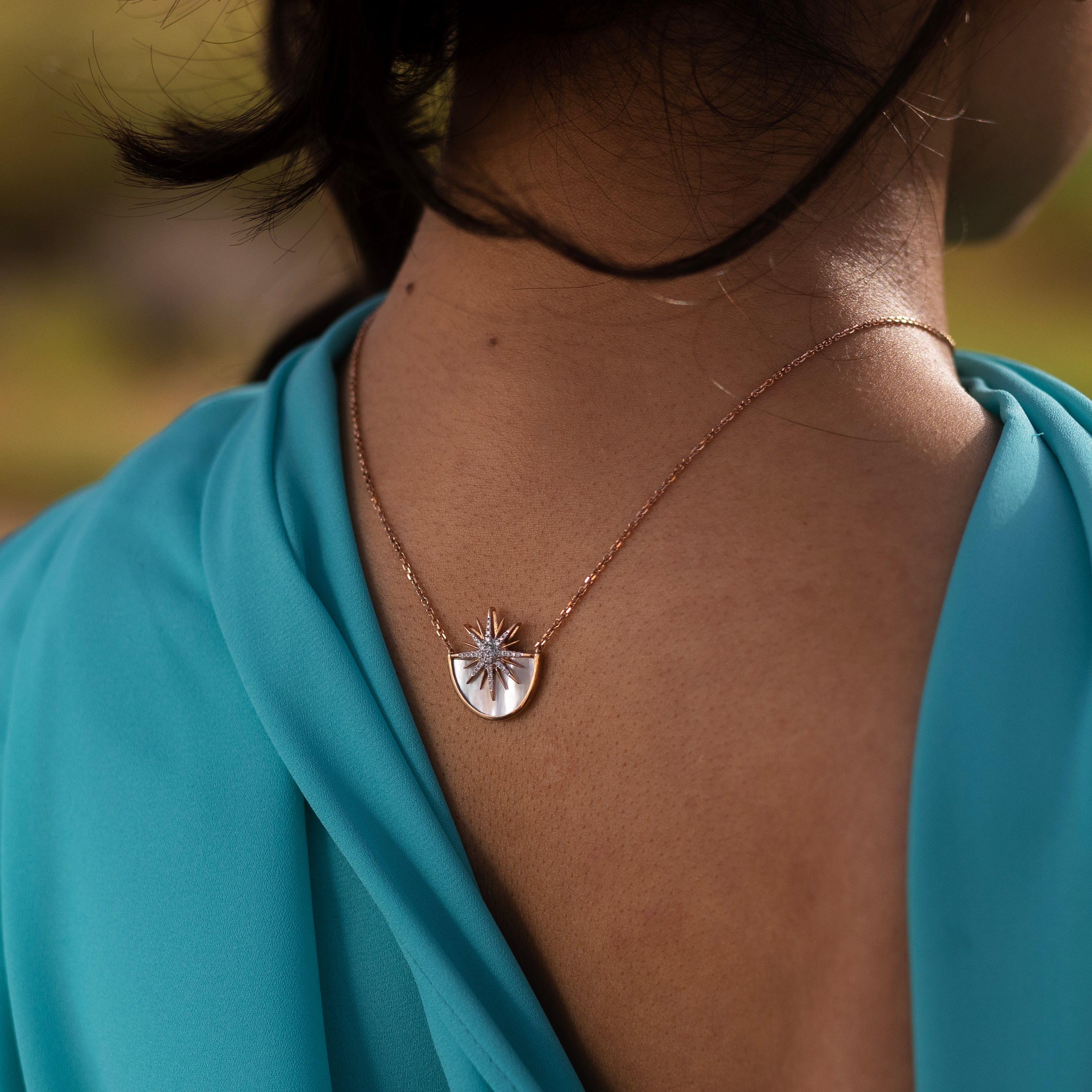 Back view of a rose gold necklace with a white mother of pearl sunshine necklace resting on the woman's back.