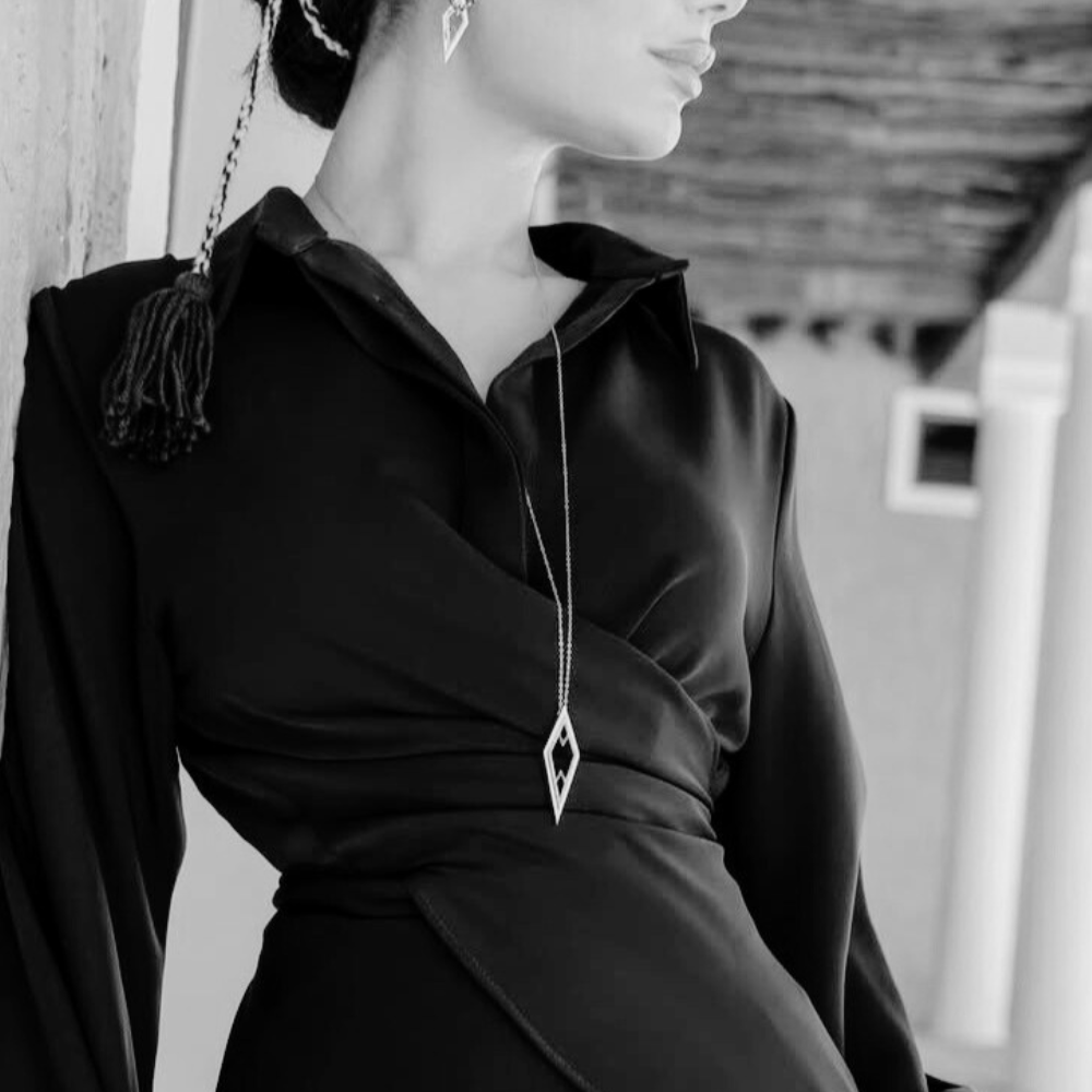 Woman wearing an elegant black outfit with a long gold necklace featuring black stones and white diamonds.