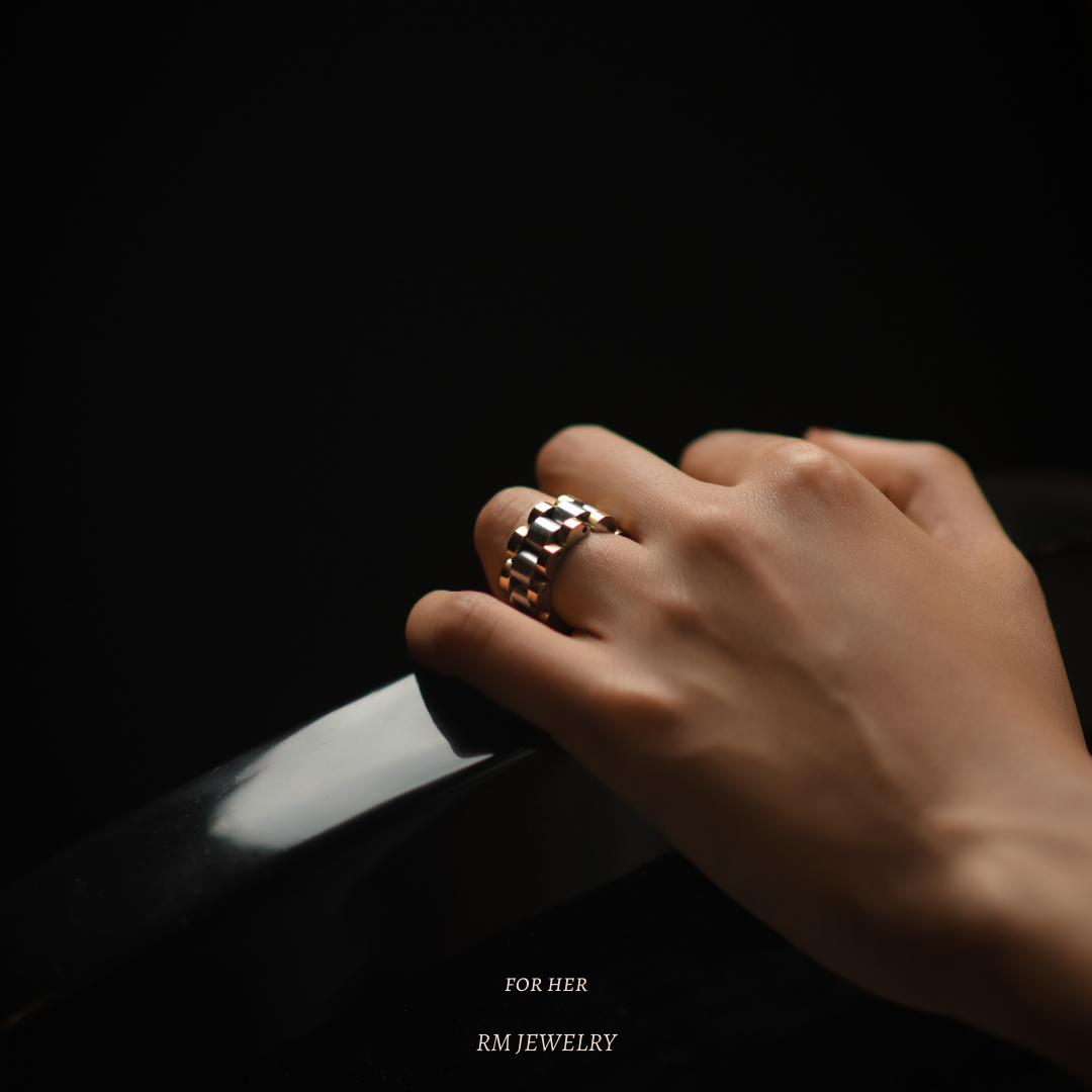 Hand wearing a bold two-tone ring from RM Jewelry, captured against a dark background with elegant lighting.